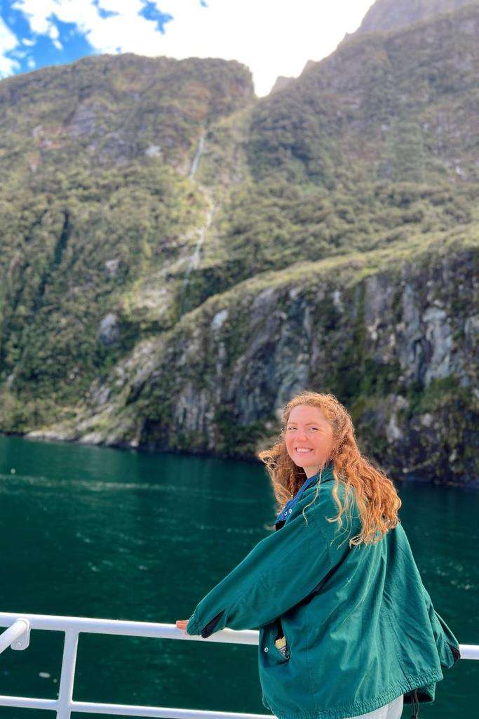 Liz standing in front of a waterfall on a boat in New Zealand.