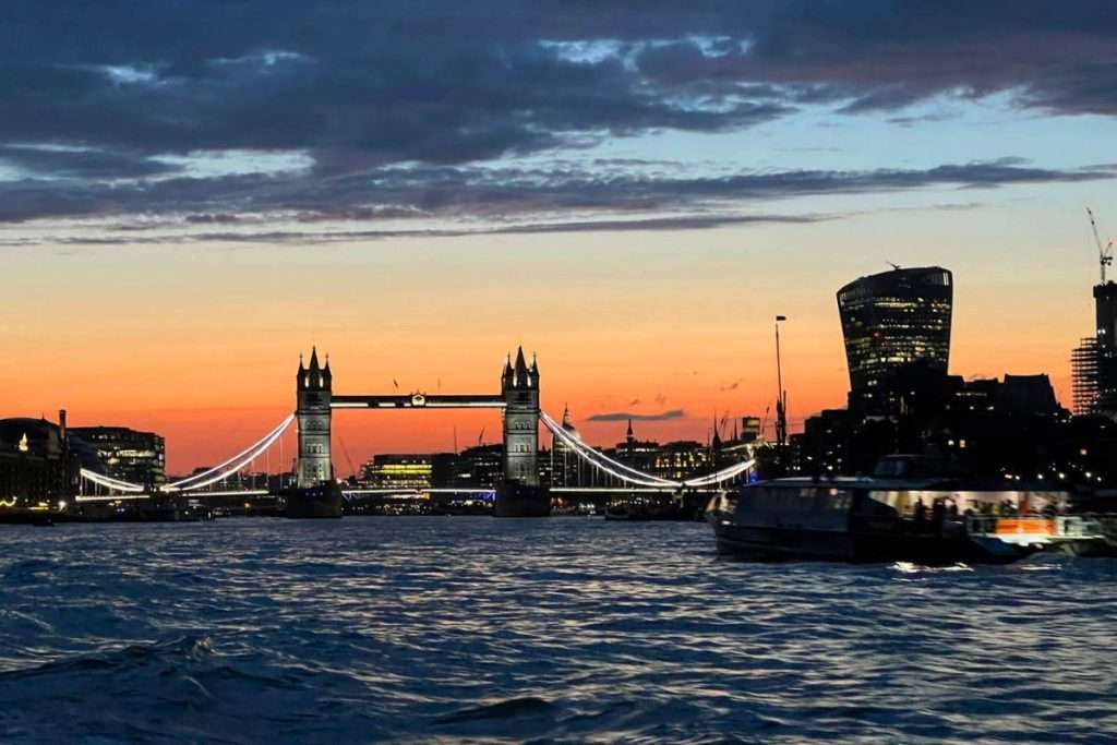 The view from an Uber boat headed towards tower bridge in London with the sun setting in the background.
