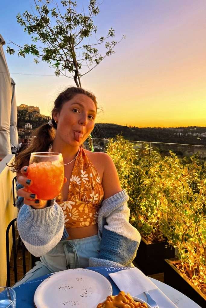 Traveler Liz with a drink at Hyper Astro Bar watching the sun set in Athens.