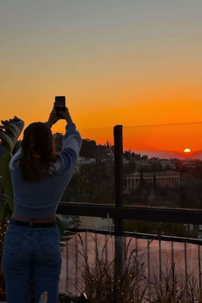 Traveler Liz taking a picture of the sun setting from a bar in Athens.