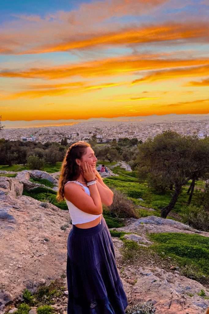 Traveler Liz staring out in the distance in awe as the sun sets behind her in Athens, Greece