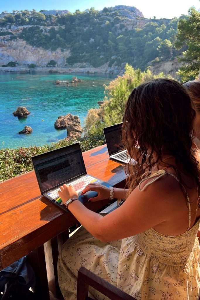 Liz working on a computer overlooking the water while traveling full-time