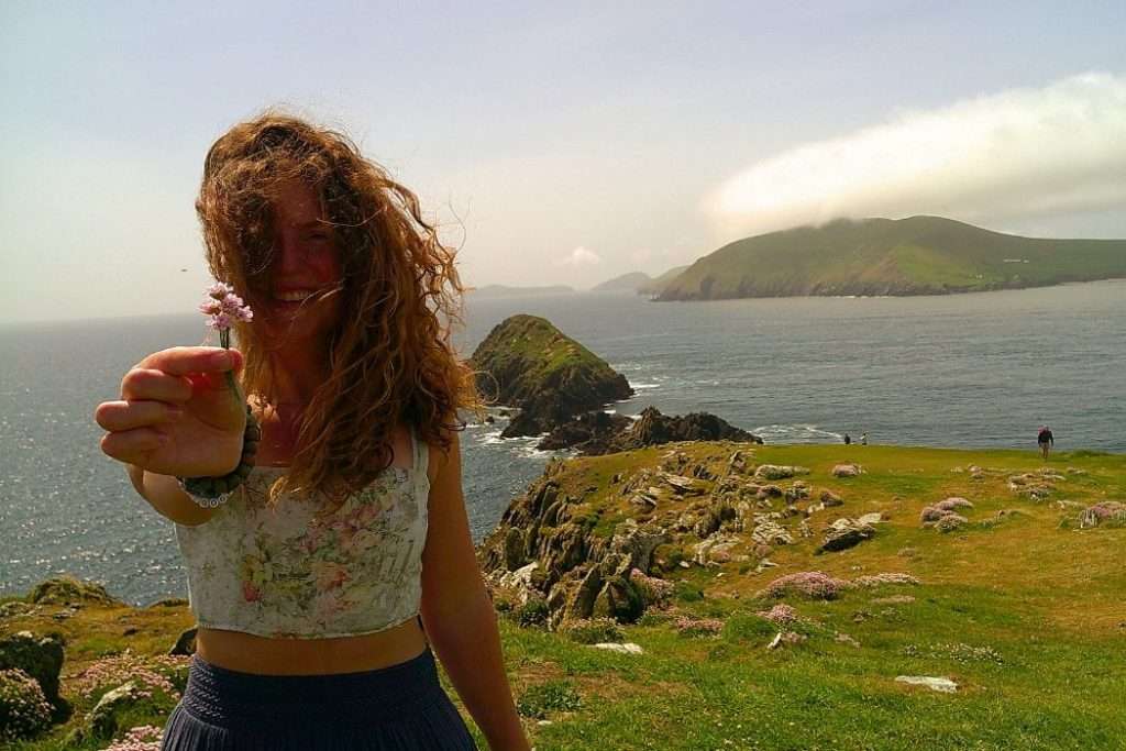 Liz holding a flower while standing on cliffs along the ocean in Ireland.